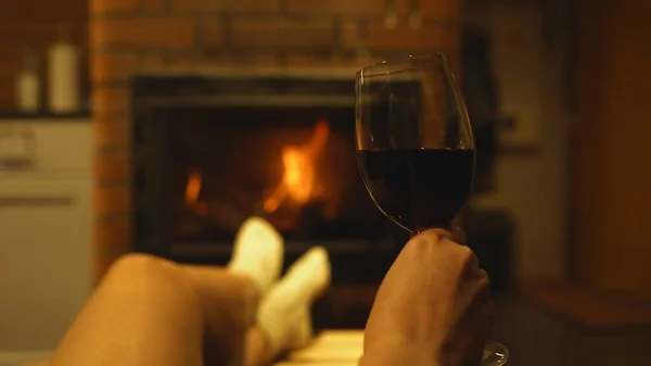 拿着红葡萄酒的女人正在壁炉边歇息 — 图库照片