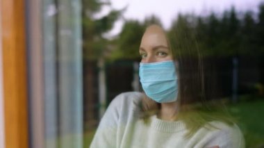 Pencerenin arkasında maskeli bir kadın var. Evde karantina.