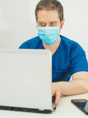 Koruyucu maskeli tıp doktoru hastasıyla görüntülü görüşme yapıyor..