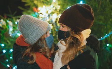 Anne ve kızı, Noel ağacının yanında koruyucu maskeler takmış..