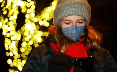 Sokakta telefonu olan koruyucu maskeli bir kız..