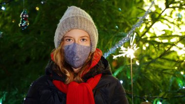 Elinde maytapla maske takan üzgün küçük kız. Covid Noelleri.