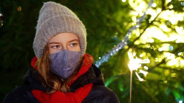 Elinde maytapla maske takan üzgün küçük kız. Covid Noelleri.