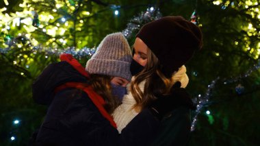 Anne ve kızı, Noel ağacının yanında koruyucu maskeler takmış..