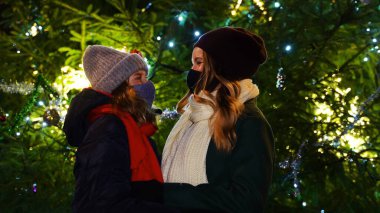 Anne ve kızı, Noel ağacının yanında koruyucu maskeler takmış..