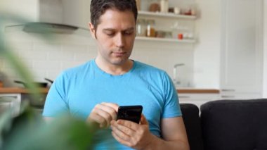 Kanepede akıllı telefonu olan yakışıklı bir adam..