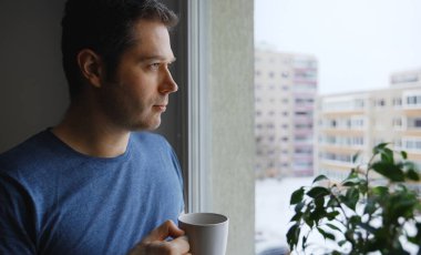 Elinde çay olan adam pencereden dışarı bakar..