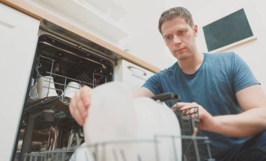 Adam mutfaktaki bulaşık makinesine tabak koyuyor..