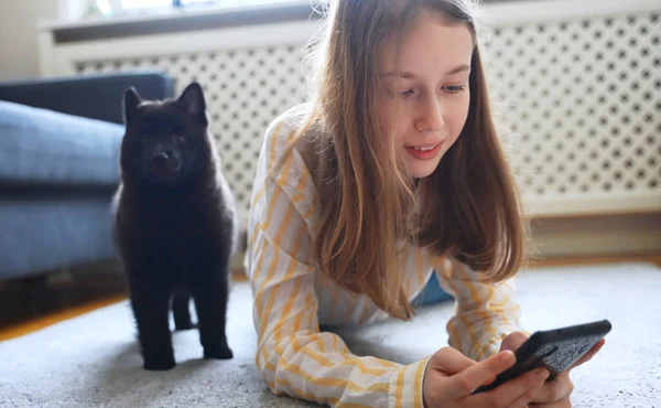 Tween girl with smartphone and curious puppy.
