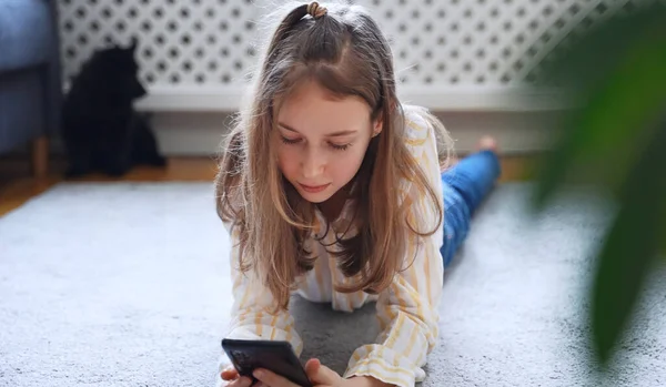 Tween girl with smartphone lying on the carpet.