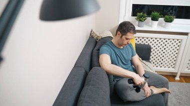 Evde masaj aleti ile bacağa masaj yapan bir adam var..