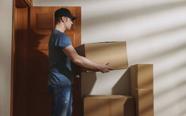 Handsome man in cap delivers cardboard boxes.
