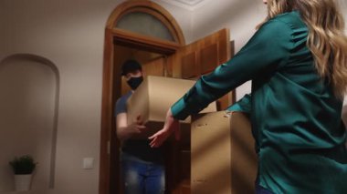 Şapkalı maskeli postacı karton kutular getiriyor..