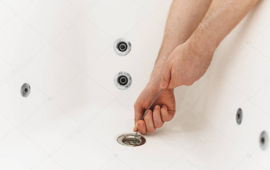 Plumber using drain snake to unclog bathtub.