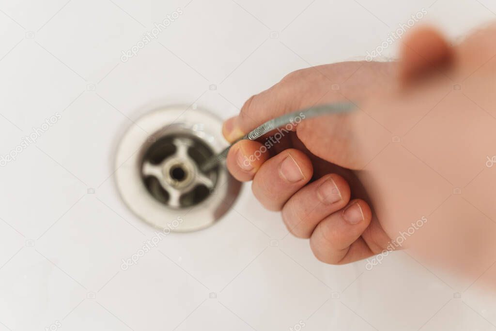 Plumber using drain snake to unclog bathtub.