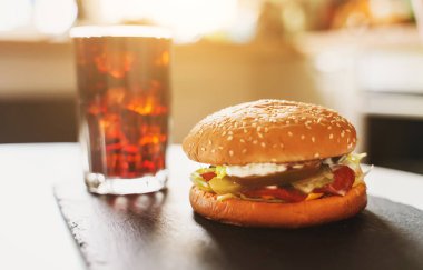 Masanın üzerinde el yapımı hamburger ve kola var..