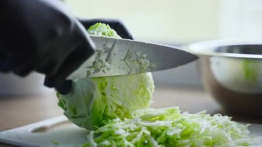 Siyah eldivenli kadın şef lahanayı bıçakla keser..