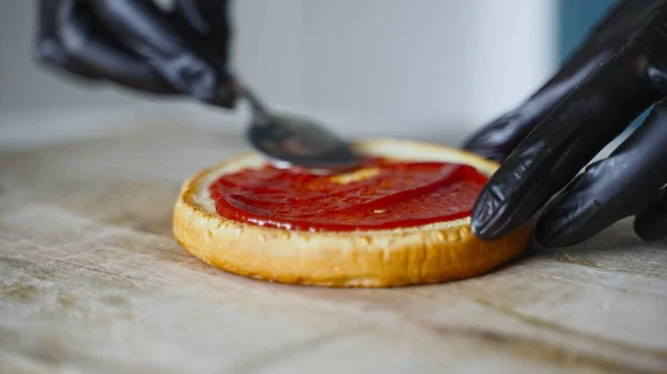 戴着黑色手套的厨师在面包上涂上番茄酱做汉堡包 — 图库照片