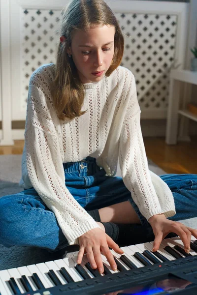 Teenage girl sitting on the floor and playing piano.
