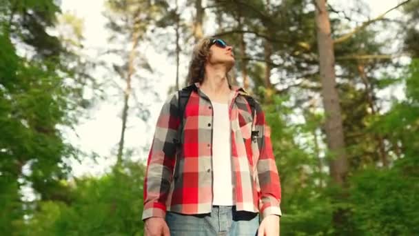 一个背着背包和太阳镜在树林里的男人弧形射击 — 图库视频影像