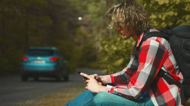 Yolun kenarında cep telefonuyla oturan erkek turist.