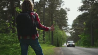 Sırt çantalı bir adam yolda araba yakalıyor. Otomatik olarak seyahat et.