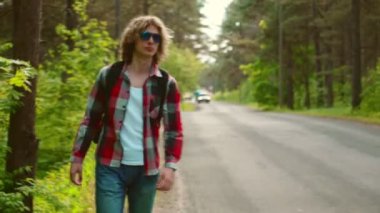 Sırt çantalı bir erkek turist yol kenarında yürüyor..