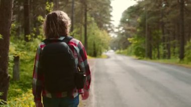 Sırt çantalı bir erkek turist yol kenarında yürüyor..