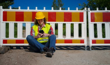 Akıllı telefon kullanan kasklı ve ceketli bir erkek işçi..
