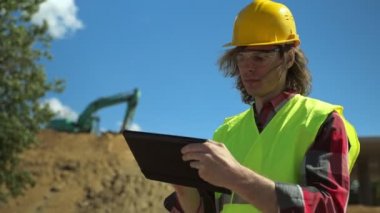 Yol kavşağı inşaat sahasında tablet bilgisayarı olan bir inşaatçı.