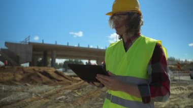 Yol kavşağı inşaat sahasında tablet bilgisayarı olan bir inşaatçı.