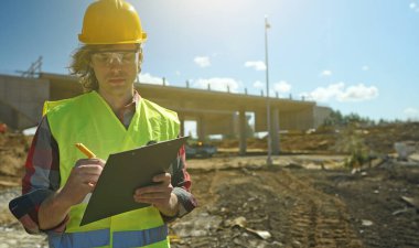 Bir yol kavşağı inşaat sahasının arka planında belgeleri olan bir inşaatçı.