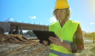 Bir yol kavşağı inşaat sahasının arka planında belgeleri olan bir inşaatçı.