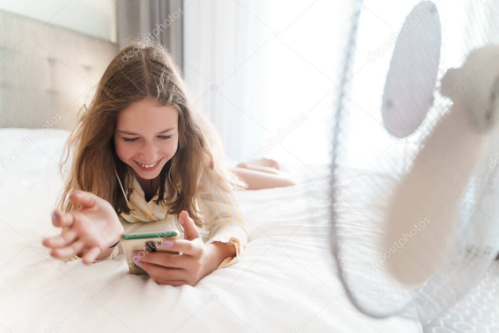Teenager lies with the phone in front of cooling fan.