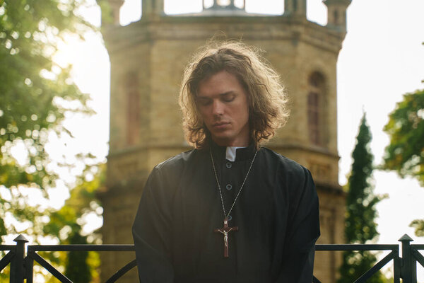 Christian priest with cross standing by the church.