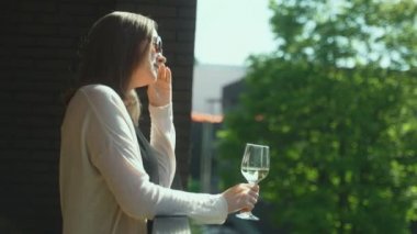 Güneş gözlüklü kadın balkonda beyaz şarap içiyor..
