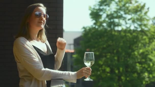 戴着太阳镜的女人在阳台上享受着白葡萄酒 — 图库视频影像
