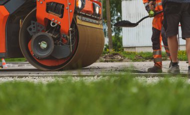 Yol yenileme. Ağır titreşimli yol silindiri sıcak asfalt yığıyor.