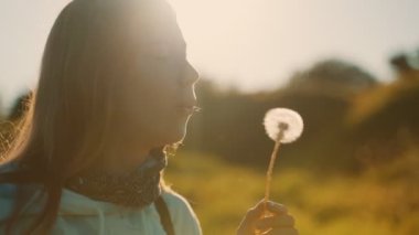 Genç kız parkta karahindiba üflüyor..