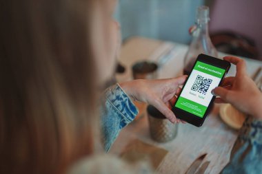 Kadın restoranda akıllı telefon uygulamasını aşılama sertifikasıyla kontrol ediyor. Durum geçerlidir.