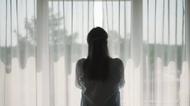 Dairesinde perdeleri açan kadın.