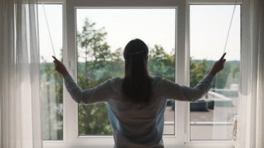 Dairesinde perdeleri kapatan bir kadın..