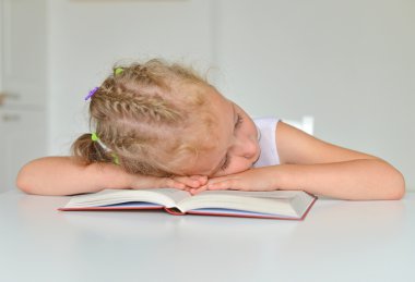 Uyuyan küçük kız masanın üzerinde kitapla.