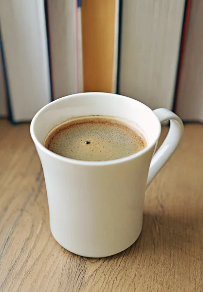 Freshly brewed coffee cup against books. — Stock Photo, Image