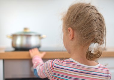 Little girl touches hot pan on the stove. Dangerous situation at home.  clipart