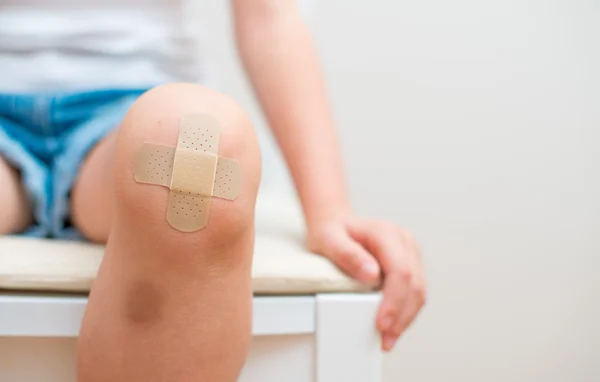 Kind knie met een zelfklevend verband en blauwe plek. — Stockfoto