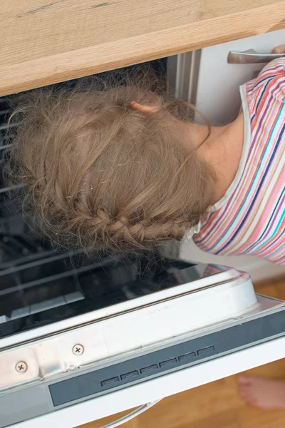 Little girl putting head into dishwasher. Dangerous situation at home. — Stock Photo, Image