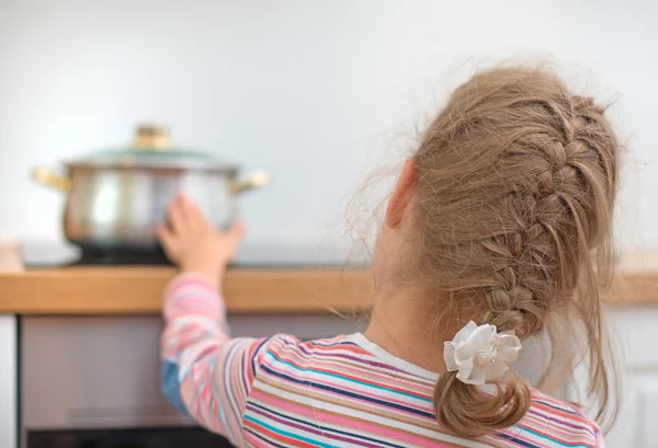 Petite fille touche poêle chaude sur la cuisinière. Situation dangereuse à la maison . — Photo