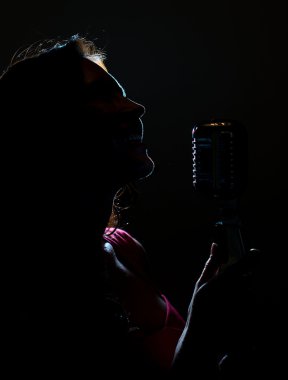 Silhouette of woman singing into vintage microphone. clipart