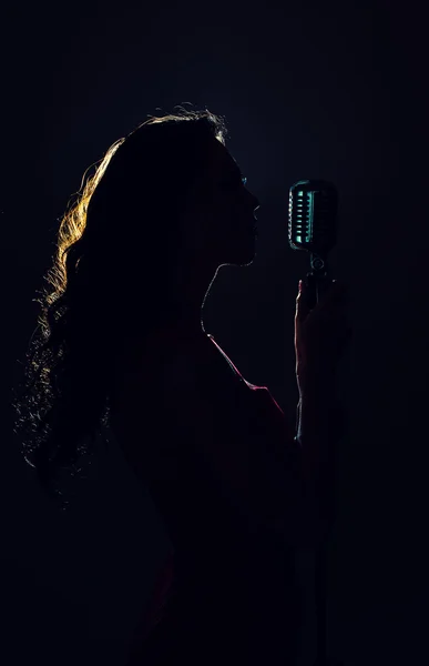 Silhouette of woman singing into vintage microphone. — Stock Photo, Image